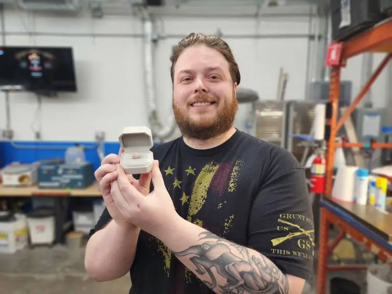 Customer smiling and holding the engagement ring he made, in its box, at the LaProng Jewelers workshop in Dallas