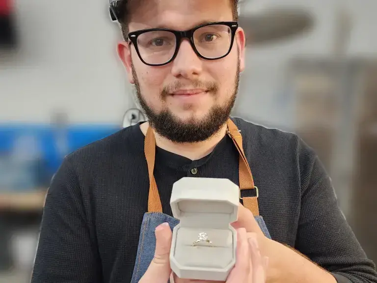 Customer smiling and holding the engagement ring he made, in its box, at a LaProng Jewelers workshop in Dallas